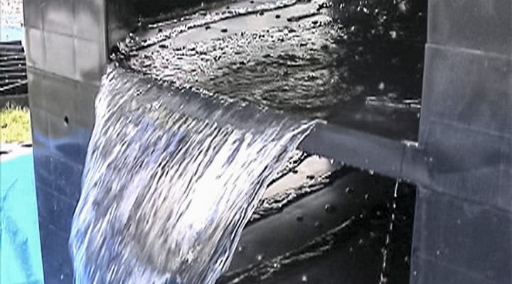 黒っぽい壁のようなところに四角く穴が空いていて、水が滝のように流れている写真
